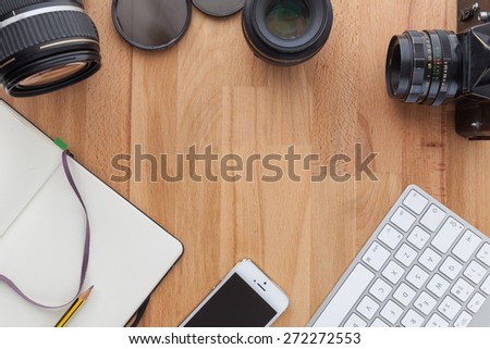 Top view of a desktop of a photographer consisting on a cameras, a keyboard, a smart phone  on a wooden desk background