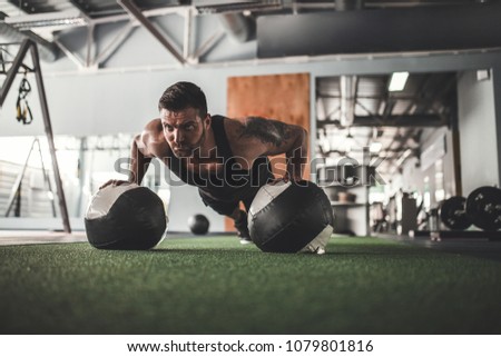Plank it. Confident bearded, tattoed muscled man wearing sport wear and doing plank position on gym balls while exercising in gym.