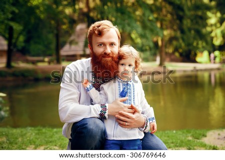 Red-heared father and red-heared son having fun in a park in a traditional white shirts with ornament