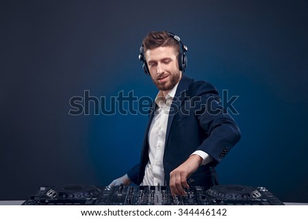 Man in dark suit play music on a DJ\'s mixer. Studio shot.