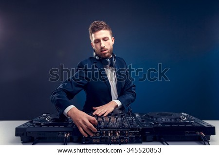 Man DJ in dark suit play music on a Dj\'s mixer. Studio shot. Dark blue background