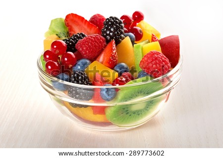 fresh fruit salad in glass bowl isolated on beige wood table
