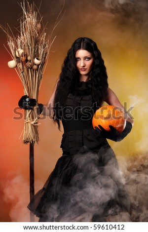 Halloween witch with a broom and carved pumpkin over color background with smoke
