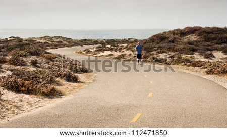 A man runs along a paved recreation trail in a sand dune area adjacent to Monterey Bay in Monterey County
