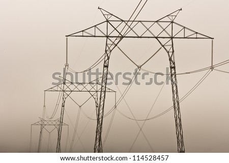 Electrical lines hang from a series of steel lattice electrical towers on a foggy morning.
