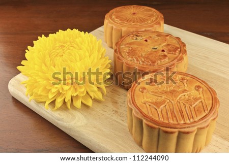 moon cakes are served with a chrysanthemum on a wooden tray.