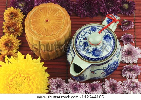 Moon cakes and tea pot on bamboo mats, decorated with colorful flowers.