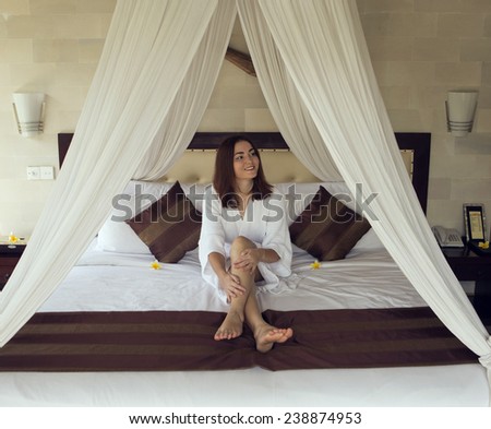 The girl smiles and irons the legs siting on a bed.
