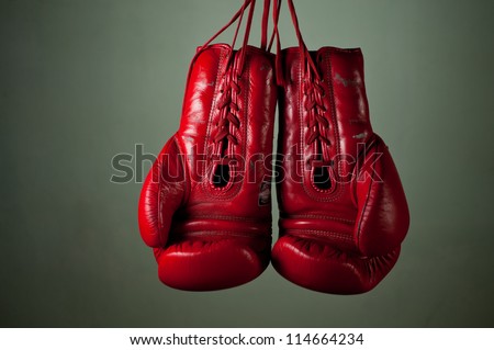 Boxing gloves hanging from laces on a grey background.