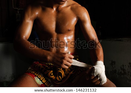 The muscular fighter tying tape around his hand preparing to fight The muscular fighter tying tape around his hand preparing to fight