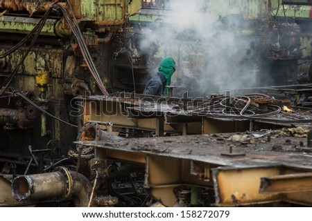 A worker uses a oxygen acetylene cutting torch to cut a large metal object in old to recycle