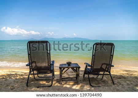 Two chairs on the beach in the shadow of a palm trees
