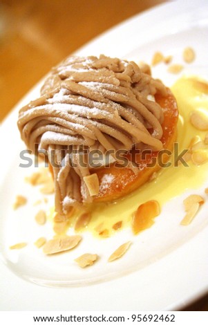 a chestnut cream cake with almond chips on a white plate with tea cup in the background