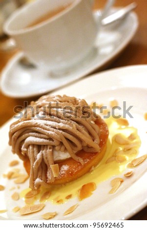 a chestnut cream cake with almond chips on a white plate with tea cup in the background