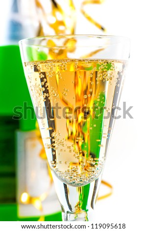 A glass of sparkling wine on the background of the bottle with a festive tinsel.