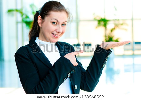 Happy young woman holding something on the palm of your hand and points a finger at her