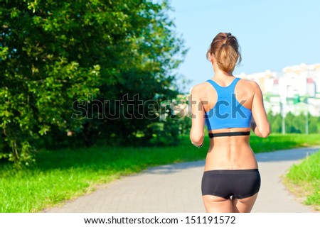 athletic girl in a top and shorts running on the road in the park, not far from the city