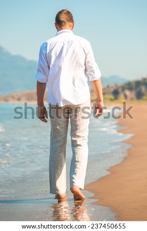 male in white clothing walking along the beach