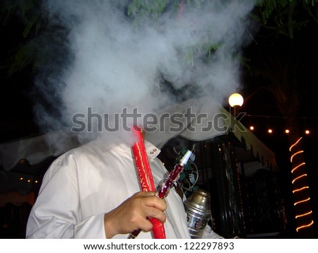 Heavy smoker - pipe man in an Arab restaurant fires up hookah pipe