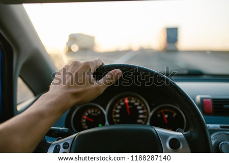 Selective focus man\'s hand on steering wheel, driving a car at sunset. Travel background