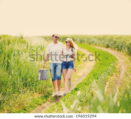 Couple walking in field,  man holding in his hand vintage suitcase, tinted photo