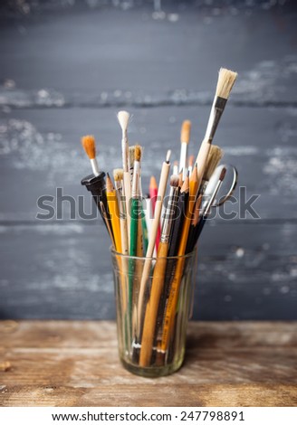 Photo of paint brushes in a glass standing on old wooden table, small dof