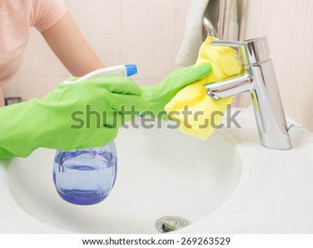 Woman doing chores in bathroom, cleaning sink and faucet with spray.