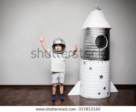 Happy child dressed in an astronaut costume playing with hand made rocket.