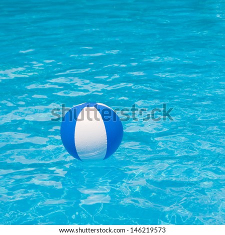 White and blue beach ball floating on a sparkling blue swimming pool