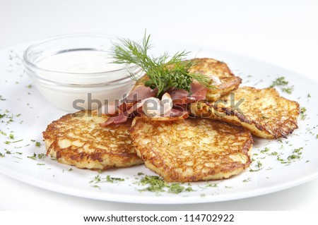 On a plate lined with fried potato pancakes with fried bacon and sour cream