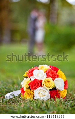 wedding flowers - Wedding bouquet of yellow and white roses and red rose lying on the grass in the park outdoors in the foreground and the couple are in blur
