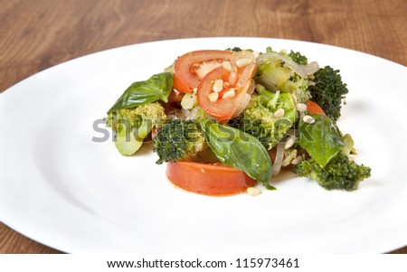 Fresh broccoli salad with lettuce, bell pepper, pine nuts,  tomatoes and onion on a white plate, which stands on a wooden table(Selective Focus, Focus on the broccoli floret in the front)