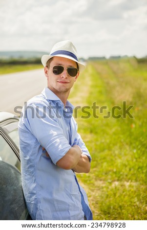 Lifestyle - guy in a summer hat standing near the car at the roadside