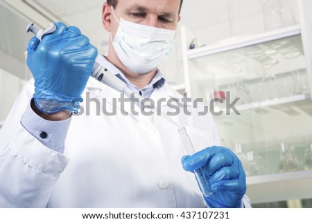 Caucasian male chemist scientific researcher in medical mask, blue rubber gloves and white coat using test tubescultivating whit inoculation loops in pipette at his workplace in the laboratory.