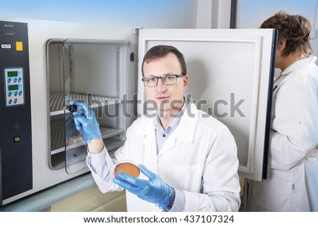 Microbiologist hand cultivating a petri dish whit inoculation loops, beside autoclave for sterilising