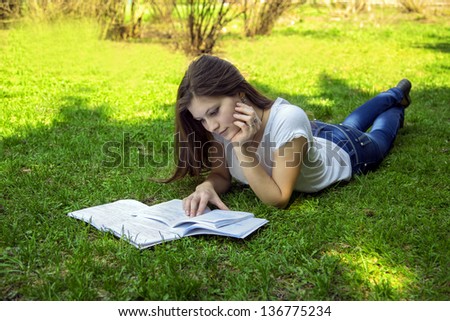 Student woman teaches from notes lying on the grass in the park