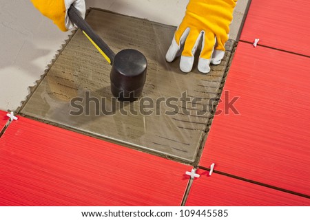 Worker with rubber hammer install glass tiles with tile adhesive.