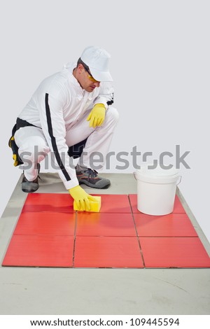 worker with yellow gloves and yellow sponge cleans red tiles from cement milk after grouting