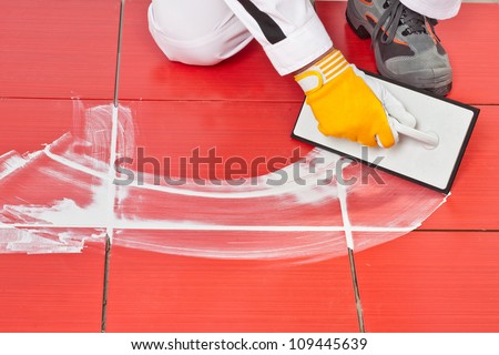 worker with rubber trowel applying white grout on red tiles on floor