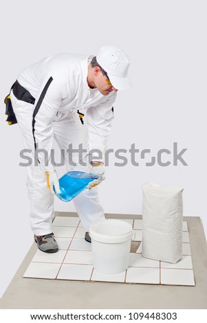 Worker mix tile adhesive in bucket of water with product package