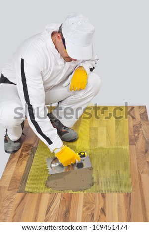 Worker applies tile adhesive with reinforcement mesh on wooden floor