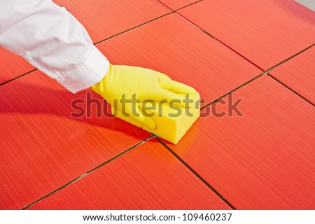 hand with yellow gloves and yellow  sponge clean red tiles