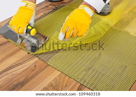 applying tile adhesive with reinforcement mesh on wooden floor