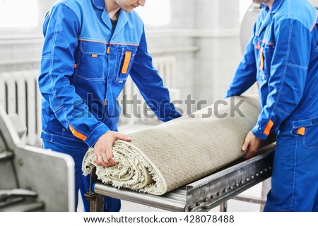 Men workers cleaning get carpet from an automatic washing machine and carry it in the clothes dryer in the Laundry room