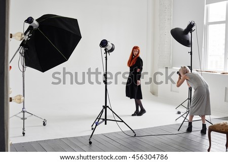 Girl the photographer takes pictures of model in black on a white background in Studio