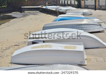 Row of boats laying on a concrete landing next to a sandy beach by the ocean.