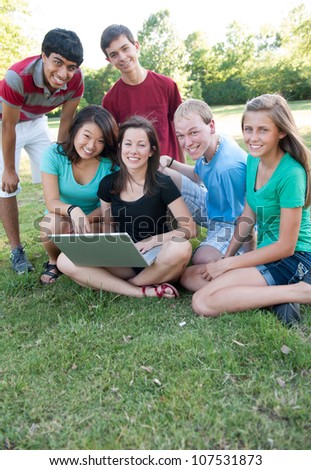 Multi-ethnic group of teens outside looking at a computer