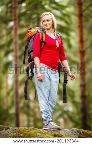 Hiker woman with backpack enjoying forest view from top of a rock.