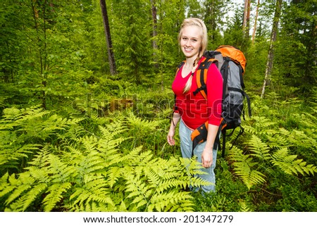 Woman hiking in summer forest. Recreation and healthy lifestyle outdoors in nature. Beauty blond looking at camera smiling.