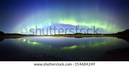 Northern lights panorama with reflection in the lake at night in Finland. Beautiful night sky and mysterious colors above still water.